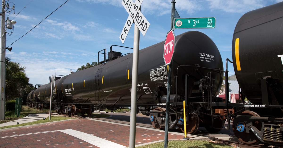 Black railroad tank cars passes over a brick unmanned crossing.