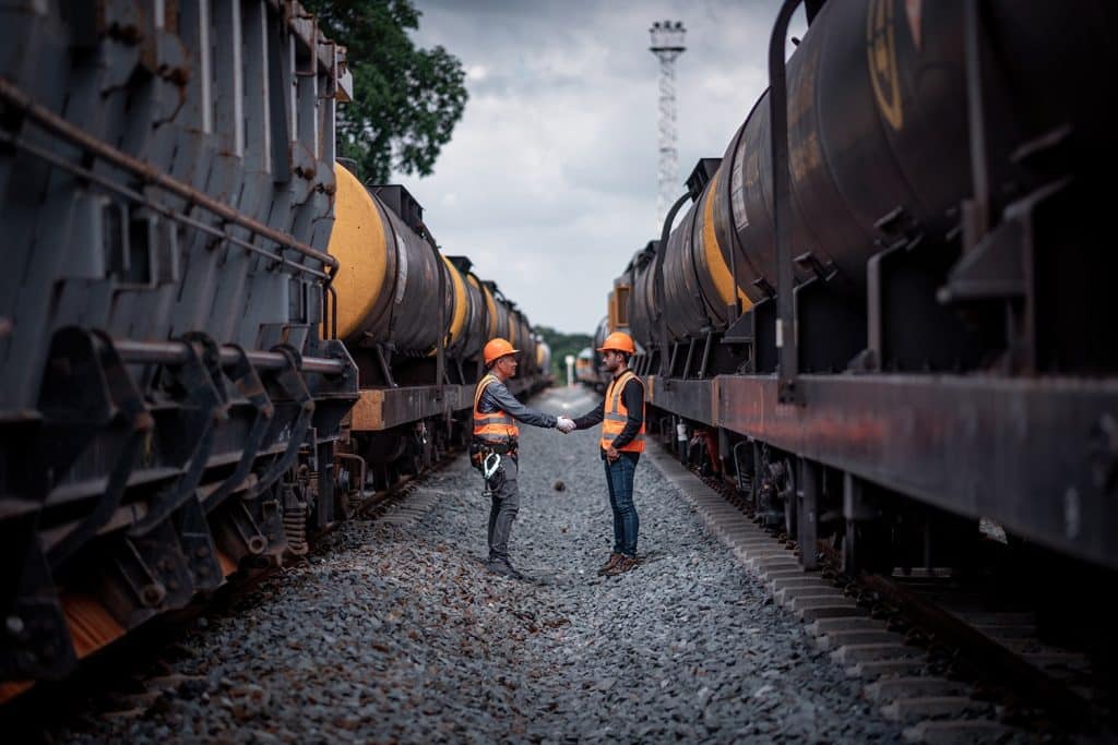 A freight rate negotiation handshake between a line of black rail tank cars.
