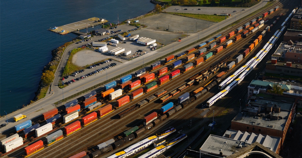 Several lines of colorful rail shipping cars at a rail yard next to a river and port.