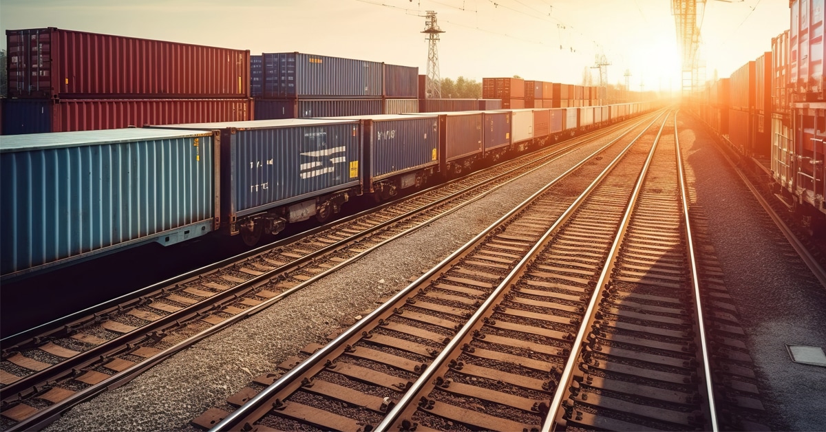 Lines of railcars and between them three lanes of rail track with a sunset behind them.