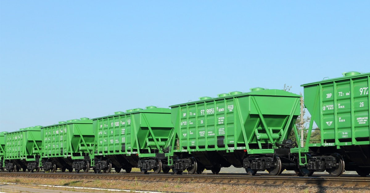 A line of green rail hopper cars against a blue sky.