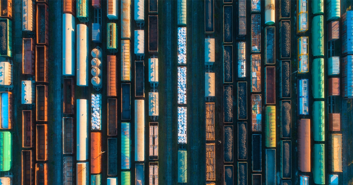 Overhead view of a railyard that is filled with lines of colorful tank cars, railcars, and hopper cars.