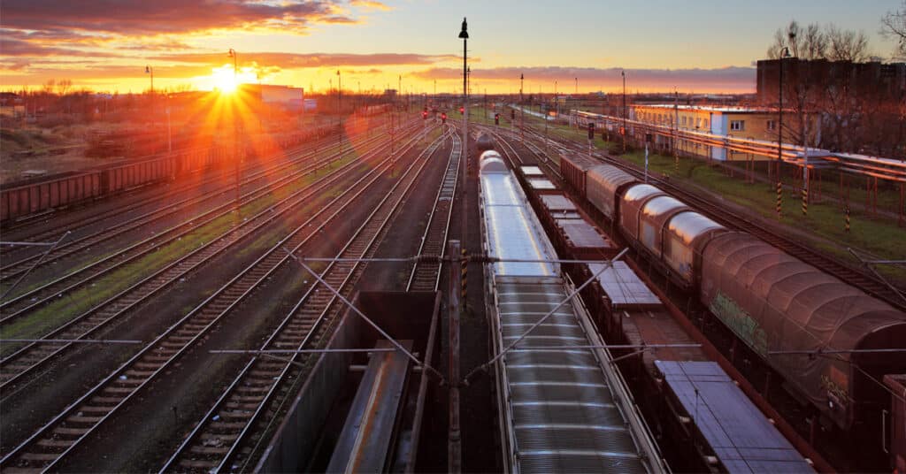 A row of railcars in a railyard with a sunset in the background.