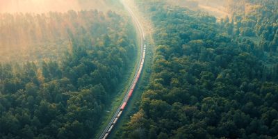 Cargo Train in summer morning forest at fog sunrise. Aerial view of moving freight train in forest.