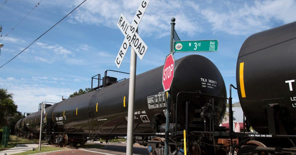 Black tank cars passing through a railroad crossing.