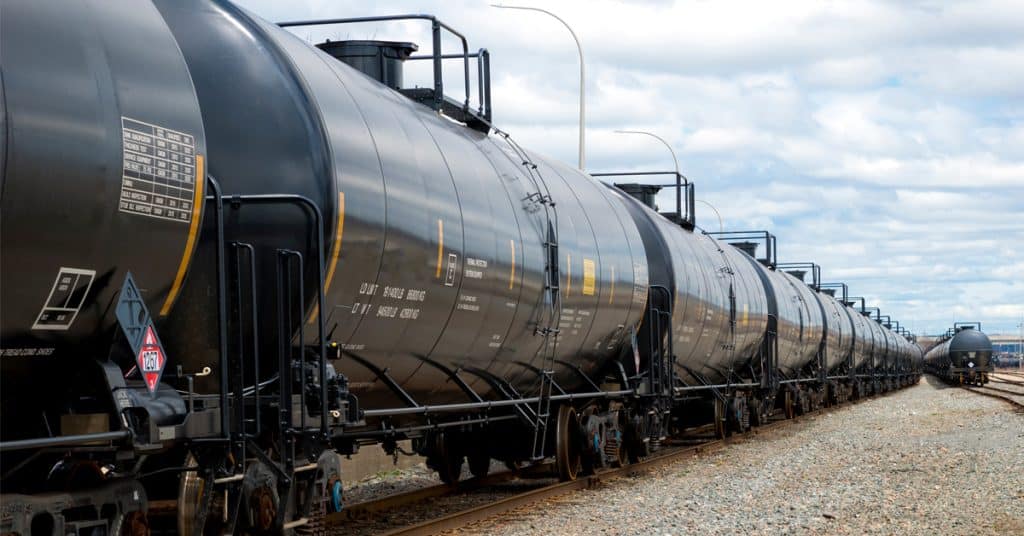 A line of black rail tank cars along a track under a blue sky.