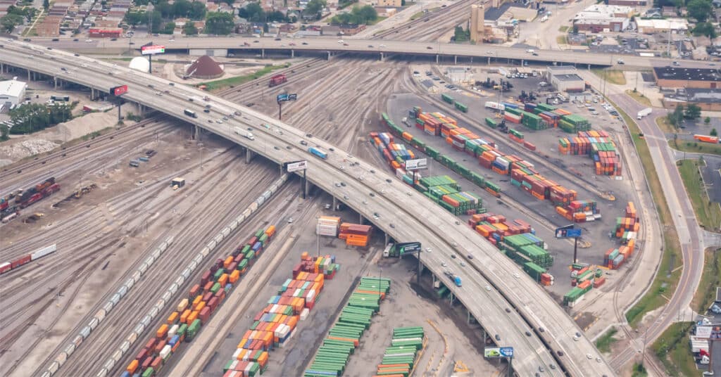 Aerial view of an Intermodel rail yard in the suburbs next to a highway system.