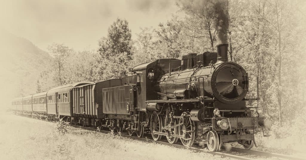 A vintage rail steam locomotive hauling rail shipping cars in a black and white photo.