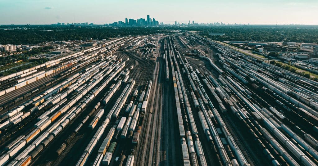 An expansive rail yard with hundreds of rail cars, in the distance is a city skyline.