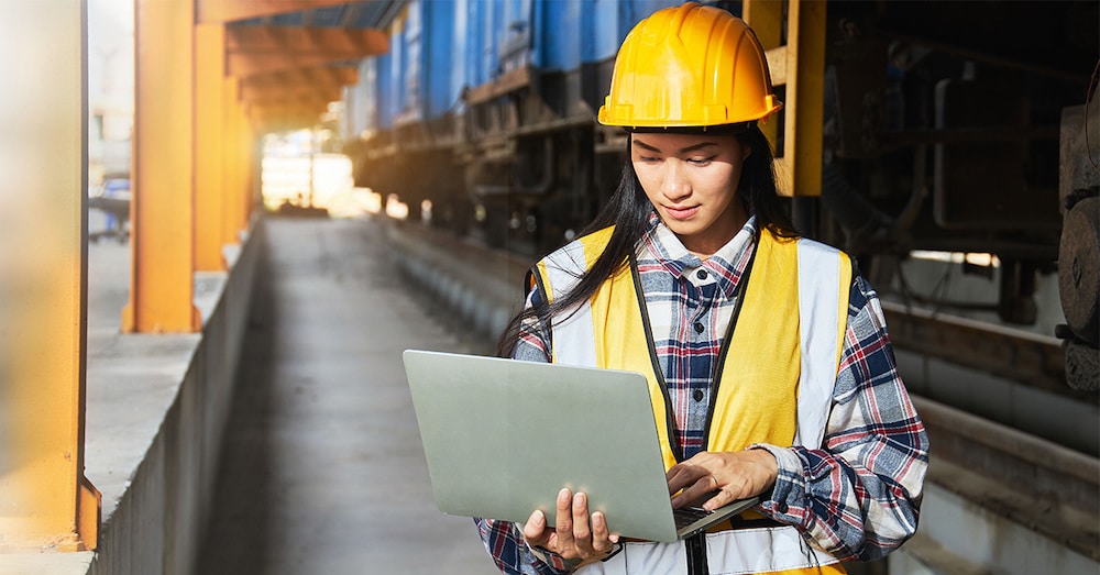 A rail logistics professional looks at rail data on a laptop in front of a railcar.