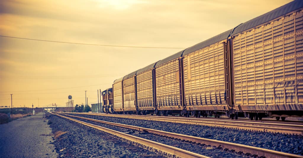 Autorack freight train traveling along tracks at sunset.