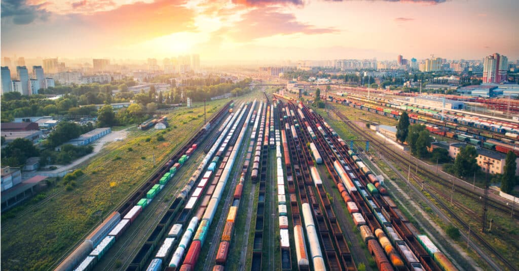 A rail yard with multiple rail cars in front of a sunset and city skyline.