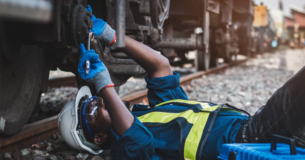 A railcar maintenance worker uses a wrench to fix a railcar.