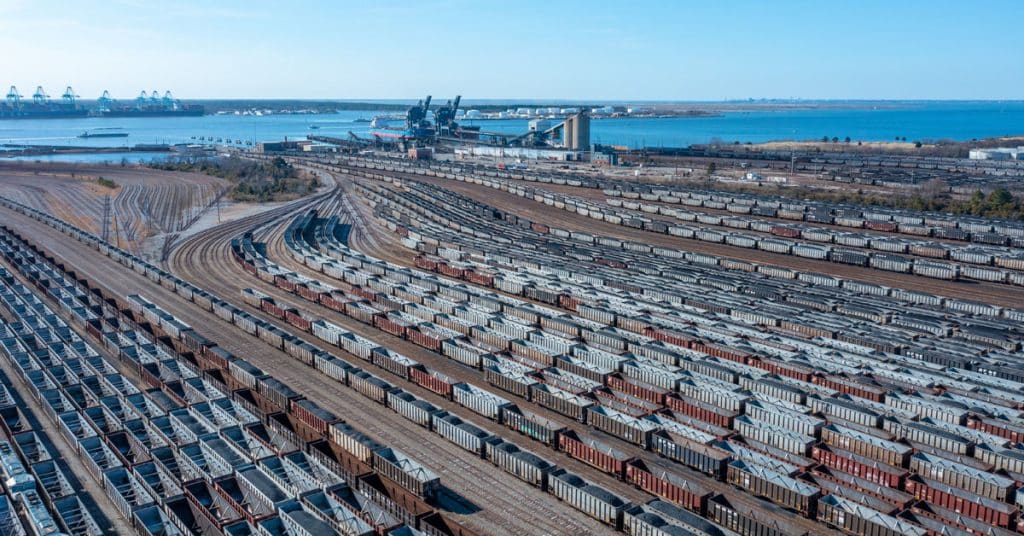 An overhead view of a factory and railcar storage yard on the edge of water.