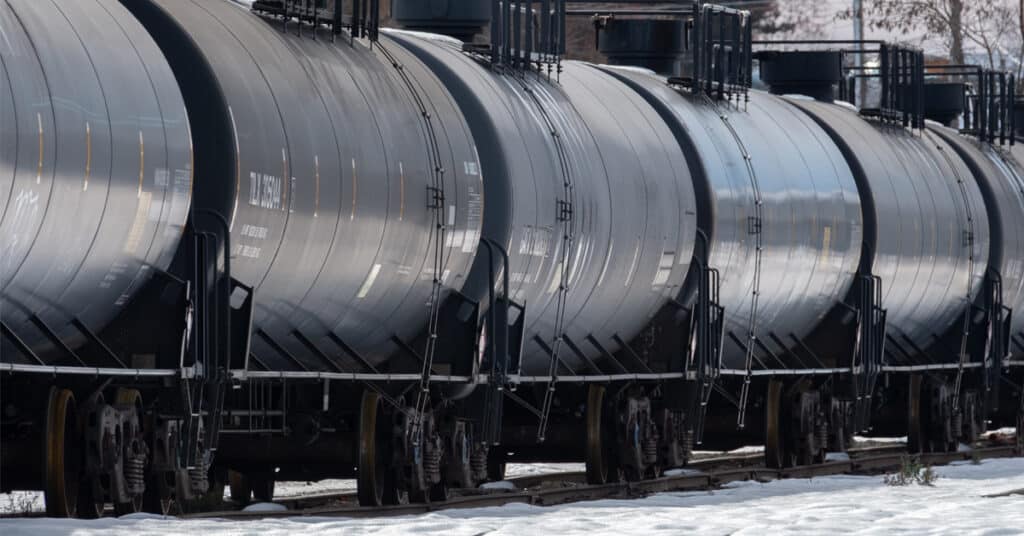 A row of black rail tank cars on a snow covered rail track.