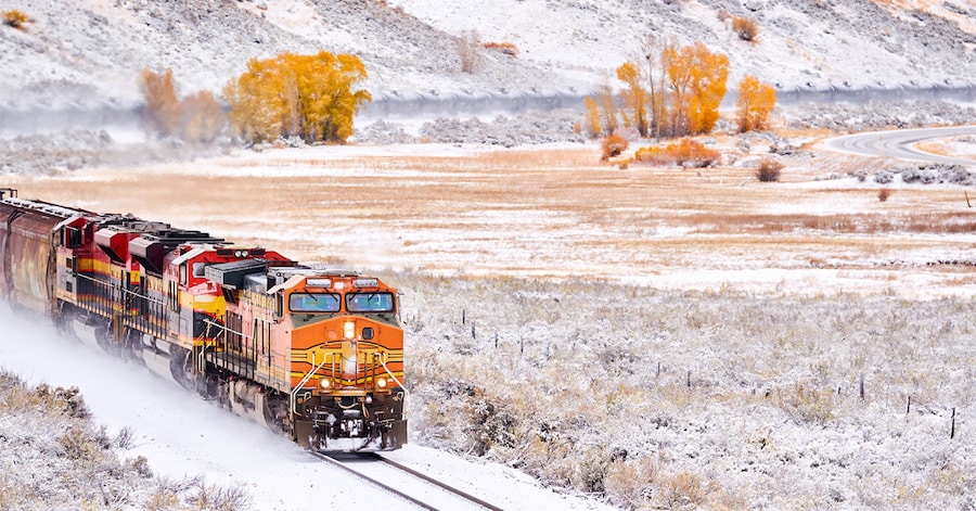 Snow covered train transporting tank cars in a snowy landscape.