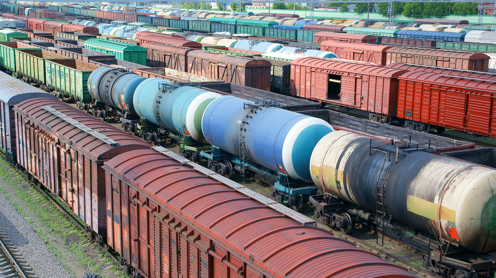 A series of colorful rail tank cars and boxcars in a rail switching yard.
